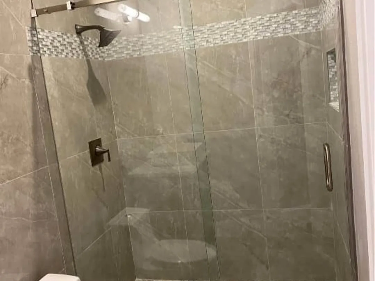 Walk in shower with large format gray tile walls, a mosaic accent band, and a sliding glass door