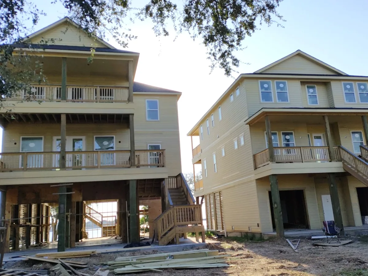 Two elevated homes under construction with yellow and blue lap siding
