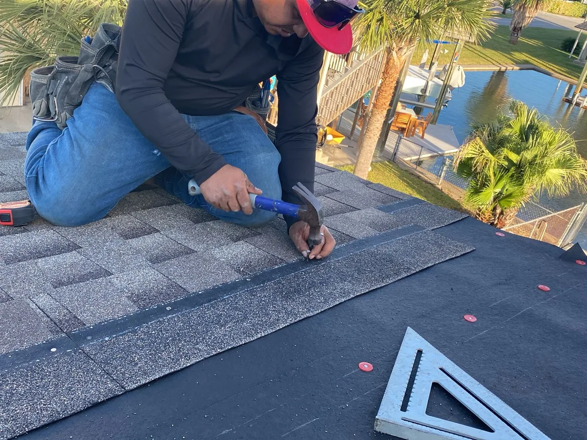 Gray asphalt shingles being nailed down course by course over a prepared roof deck